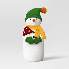 a snowman with a yellow scarf and green hat holding a mushroom in his hands