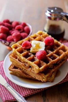 some waffles are on a plate with raspberries and syrup in the background