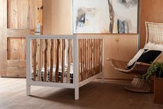 a baby crib in the corner of a room with wood paneling and paintings on the wall