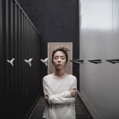 a woman standing in an empty hallway with birds flying around her and looking at the camera