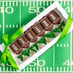 chocolate covered football cookies in a box on a green tablecloth with ribbon around the edge