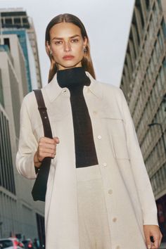 a woman in a white coat and black tie is walking down the street with her hand on her hip