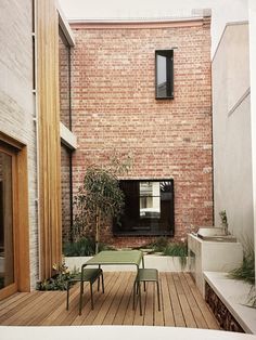 a wooden deck with green chairs and tables next to a brick building on the other side