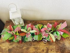 a wooden table topped with green and red christmas wreaths next to a white lantern