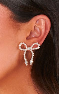 a woman wearing an earring with pearls and bows on the back of her ear