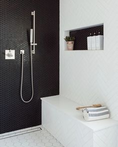 a modern bathroom with black and white tiles on the walls, shower head, and shelf