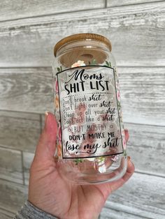 a person holding up a glass jar with some writing on the bottom and flowers in it