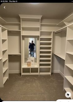 an empty walk - in closet with shelves and a man standing in the mirror looking at his reflection