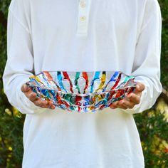 a man is holding a bowl with many colors on it in front of some trees