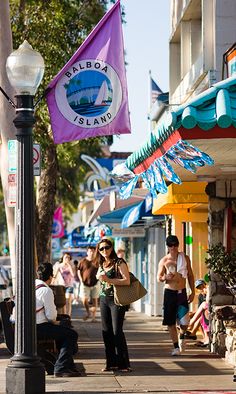 people are walking down the sidewalk in front of shops and businesses on a sunny day