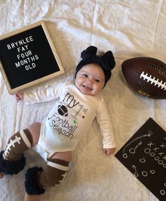 a baby laying on top of a bed next to an american football and a sign