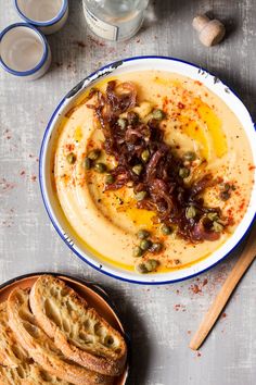 a bowl of hummus with olives and capers next to some crackers