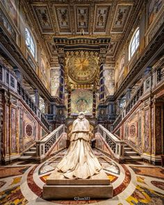 a statue in the middle of a large room with stairs and paintings on the walls