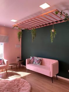 a living room with pink furniture and hanging plants on the green wall above it, along with wooden flooring