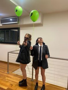 two girls dressed in school uniforms holding green balloons and looking up at the sky with their eyes closed