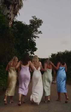 four women in dresses walking down a dirt road