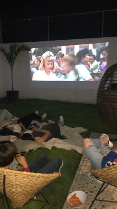 people sitting on the grass in front of a projection screen watching movies and eating food