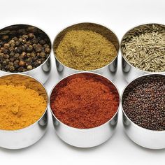 six different spices in metal containers on a white background