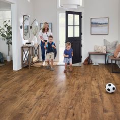 a woman and two children standing in a living room with a soccer ball on the floor