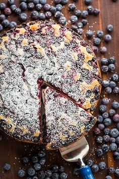 a blueberry pie with one slice cut out on a wooden table surrounded by fresh blueberries