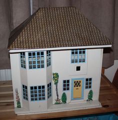 a doll house on a wooden table in front of a curtained window with blue trim