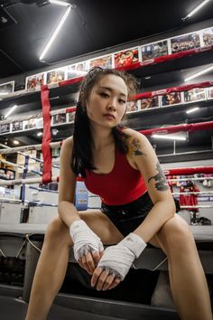 a woman sitting on top of a bench in a boxing ring wearing gloves and tattoos