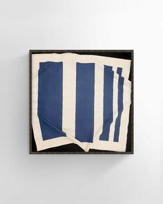 three pieces of blue and white art hanging on a wall in a black frame with one piece torn off