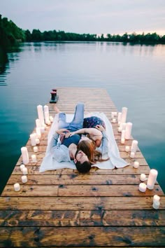 two people are laying on a dock with candles around them and one person is kissing the other