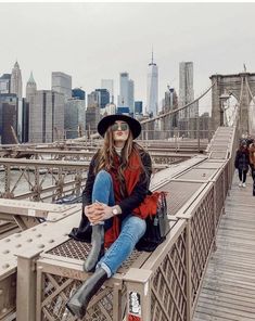 a woman sitting on the edge of a bridge with her legs crossed and wearing boots