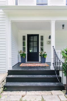 a black door and steps leading to a white house with potted plants on either side