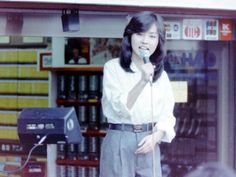 a woman standing in front of a store holding a microphone and talking into a mic