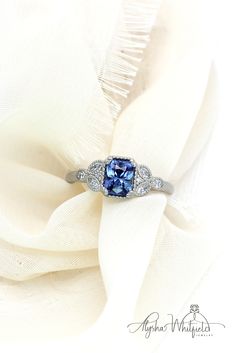 a blue and white diamond ring sitting on top of a white cloth covered tablecloth