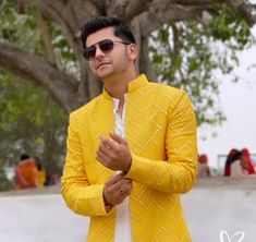 a man in a yellow jacket and white shirt is standing near a tree with sunglasses on