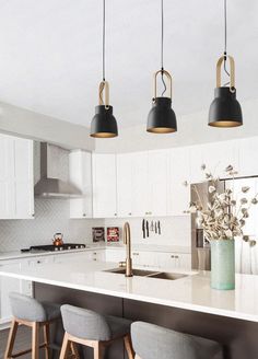 three lights hanging over a kitchen island with white counter tops and stools next to it