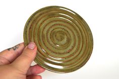 a hand is holding a green plate with brown designs on it and the other hand is pointing at it