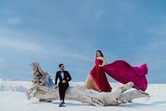 a man and woman standing next to each other near a tree trunk in the snow