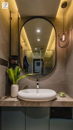 a bathroom sink sitting under a round mirror next to a green plant in a vase