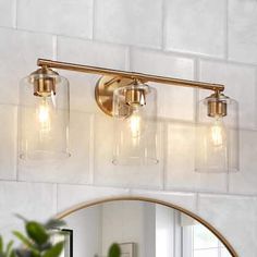 a bathroom vanity light with three lights and a round mirror on the wall above it