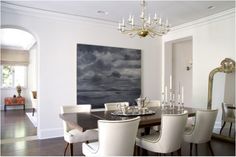 a dining room table with white chairs and a painting on the wall