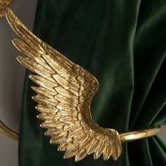 the gold wings are attached to the green velvet drapes in front of a mirror