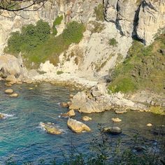 there are many rocks in the water by the cliff side and trees on the other side