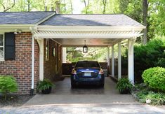 a car is parked in front of a house with a pergolated roof and brick driveway