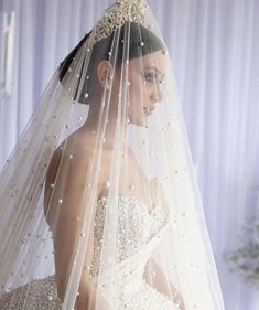 a woman in a wedding dress with a veil over her head and pearls on it