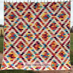 a colorful quilt hanging from a clothes line on a clothes line with the words busy hands quilts written across it