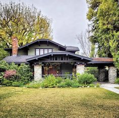 a house that is in the middle of some trees and grass with bushes around it