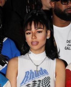 a close up of a person wearing a white shirt and some people in the background