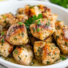 a white bowl filled with cooked chicken and garnished with parsley on top