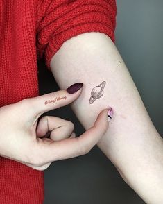 a woman's arm with a small saturn tattoo on the left side of her body