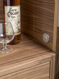 a bottle of wine sitting on top of a wooden shelf next to a glass filled with liquid