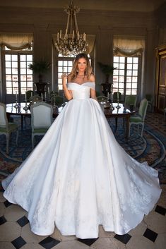 a woman in a white wedding dress standing next to a chandelier and table